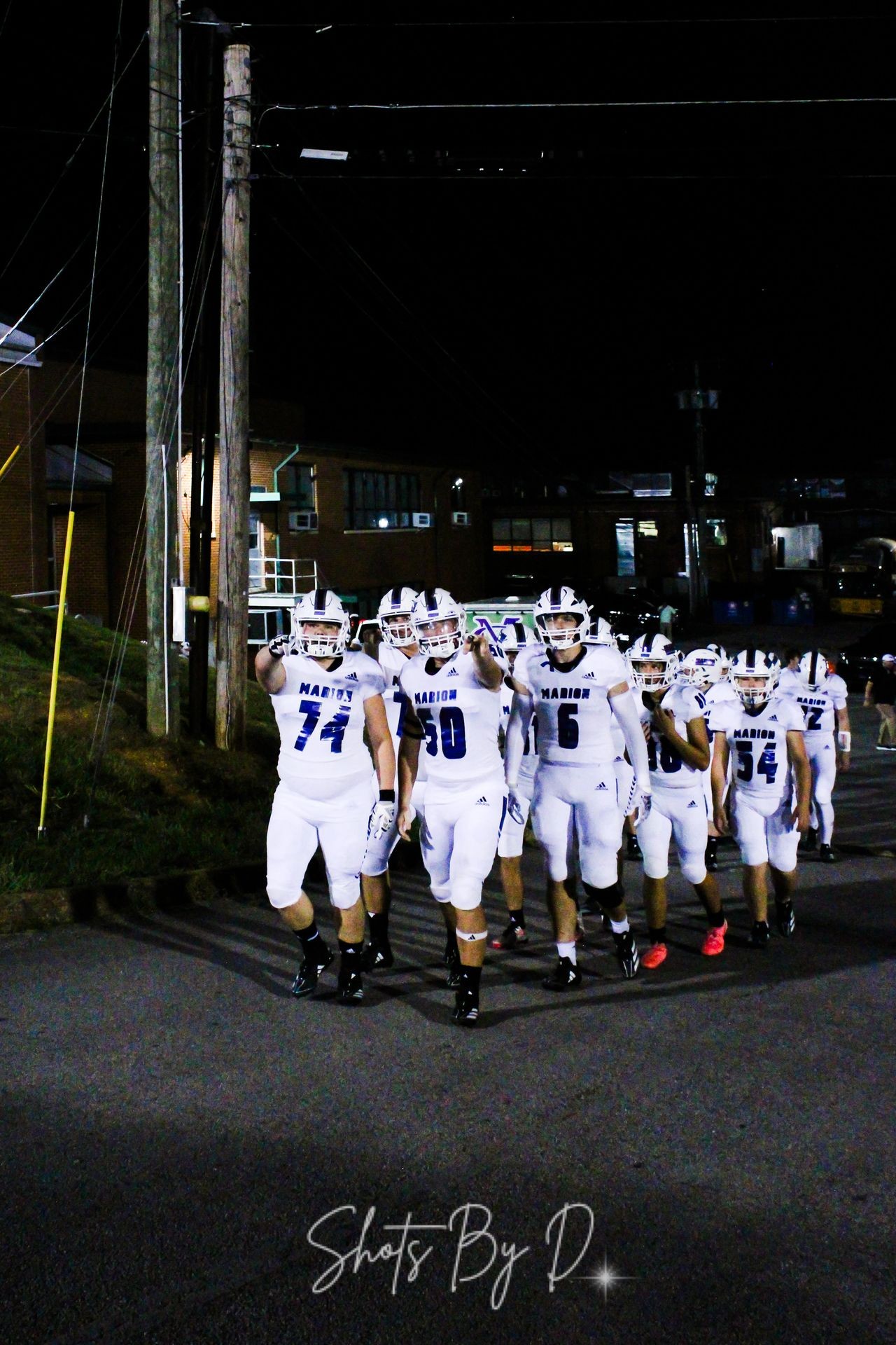 Group of football players in white uniforms walking together at night near a building with illuminated windows.