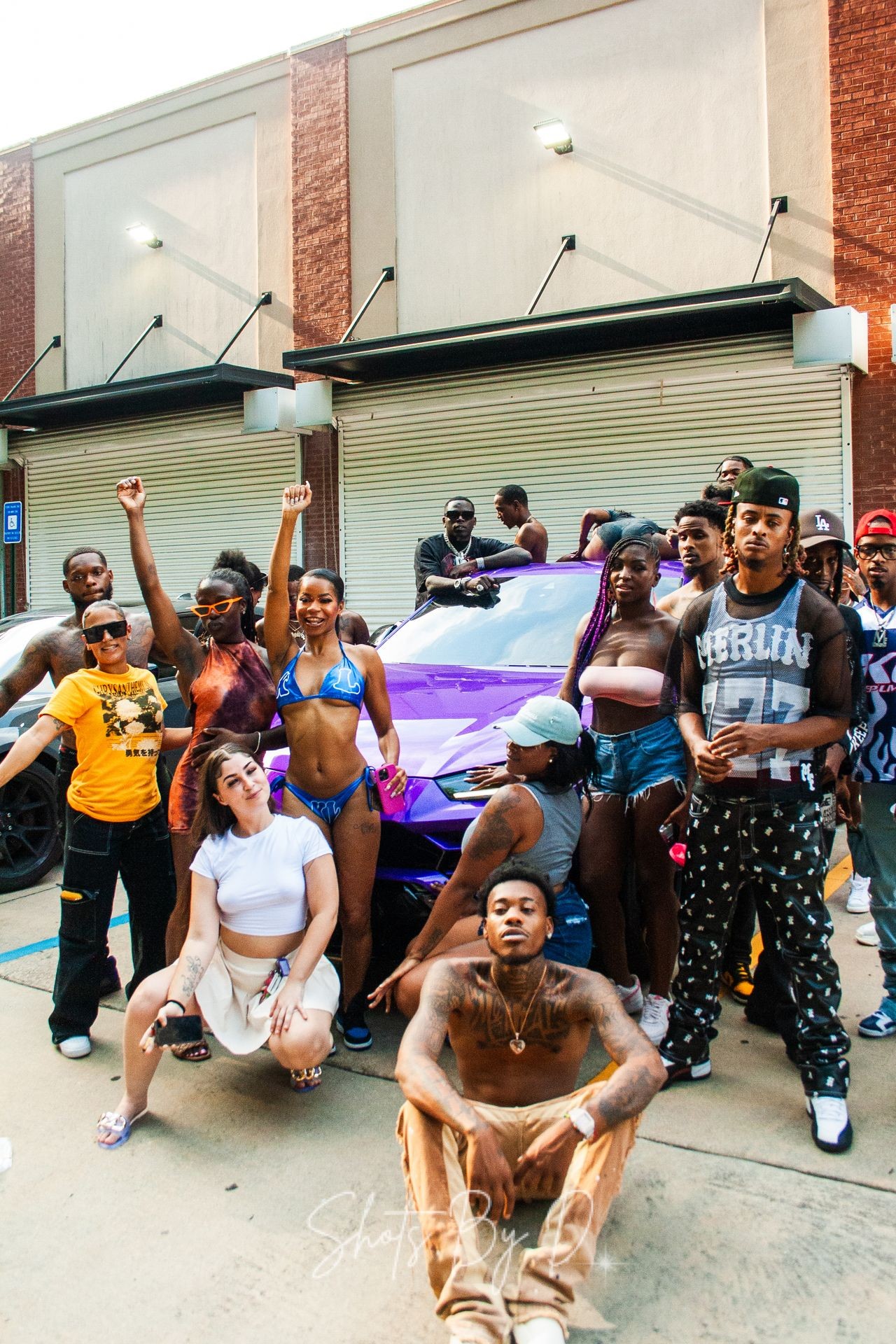 Group of people posing in front of a vibrant purple car with garage doors in the background.