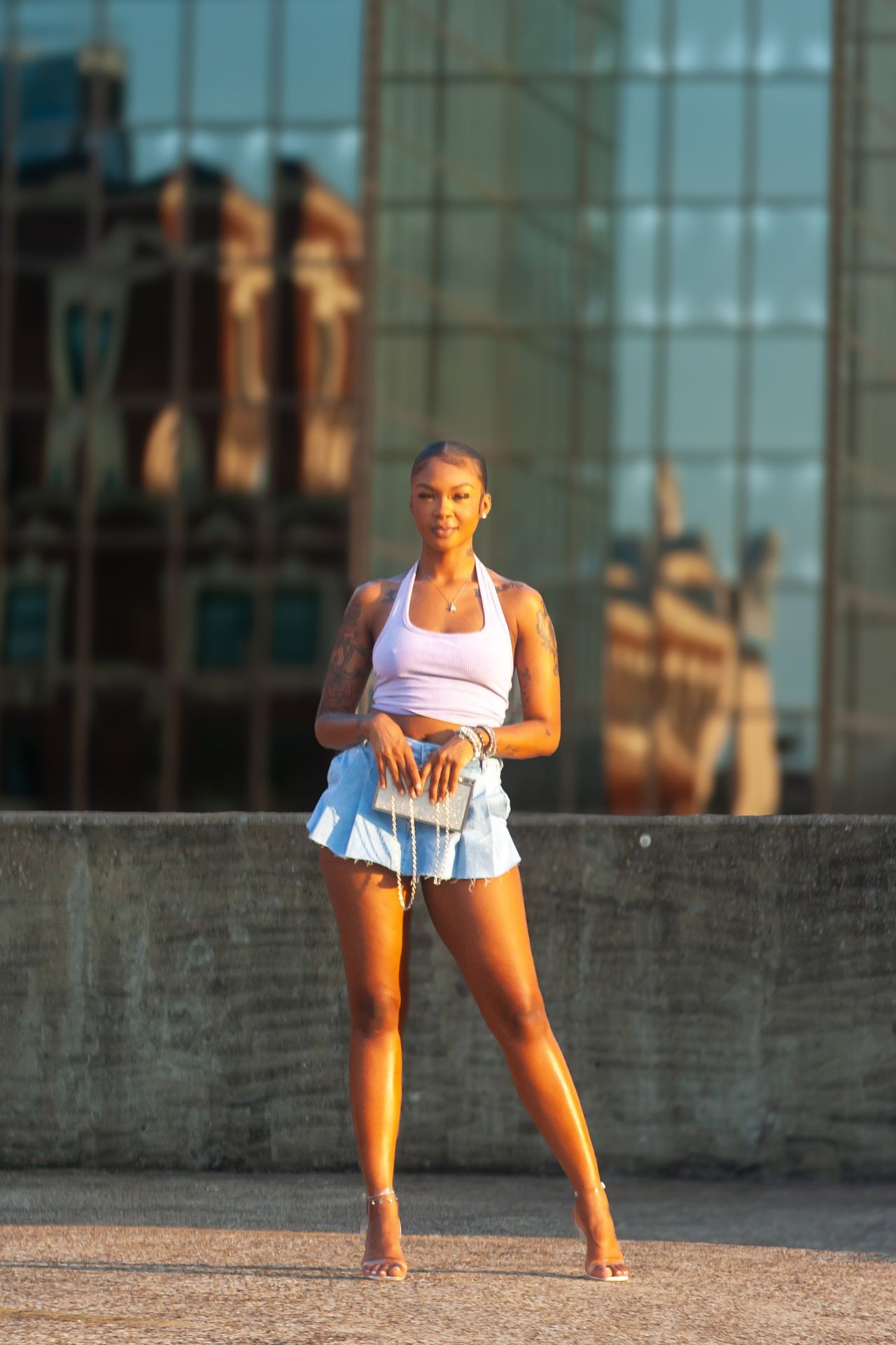 Person in a white crop top and denim skirt standing in front of a reflective building.