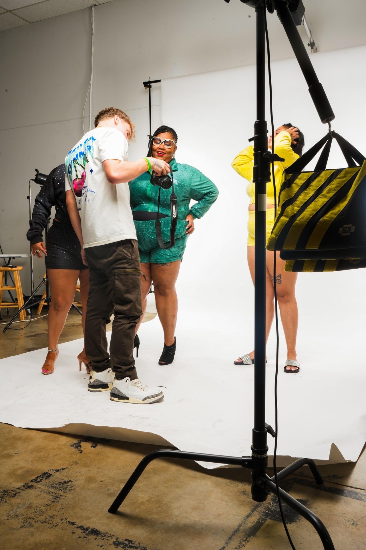 Photographer and models preparing for a photoshoot in a studio with white background and lighting equipment.